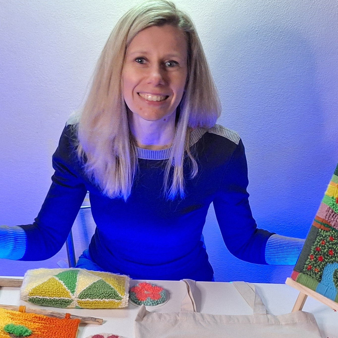 foto di Silvia seduta al tavolo dove si intravedono alcuni ricami con il punch needle