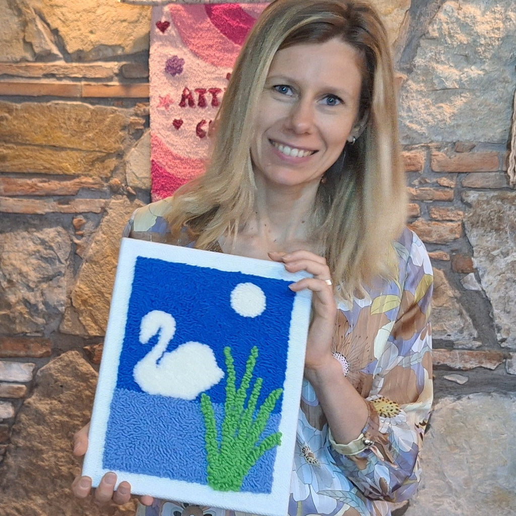 Silvia che tiene in mano il quadro ricamato con il punch needle che raffigura un cigno bianco su acqua azzurra e cielo blu