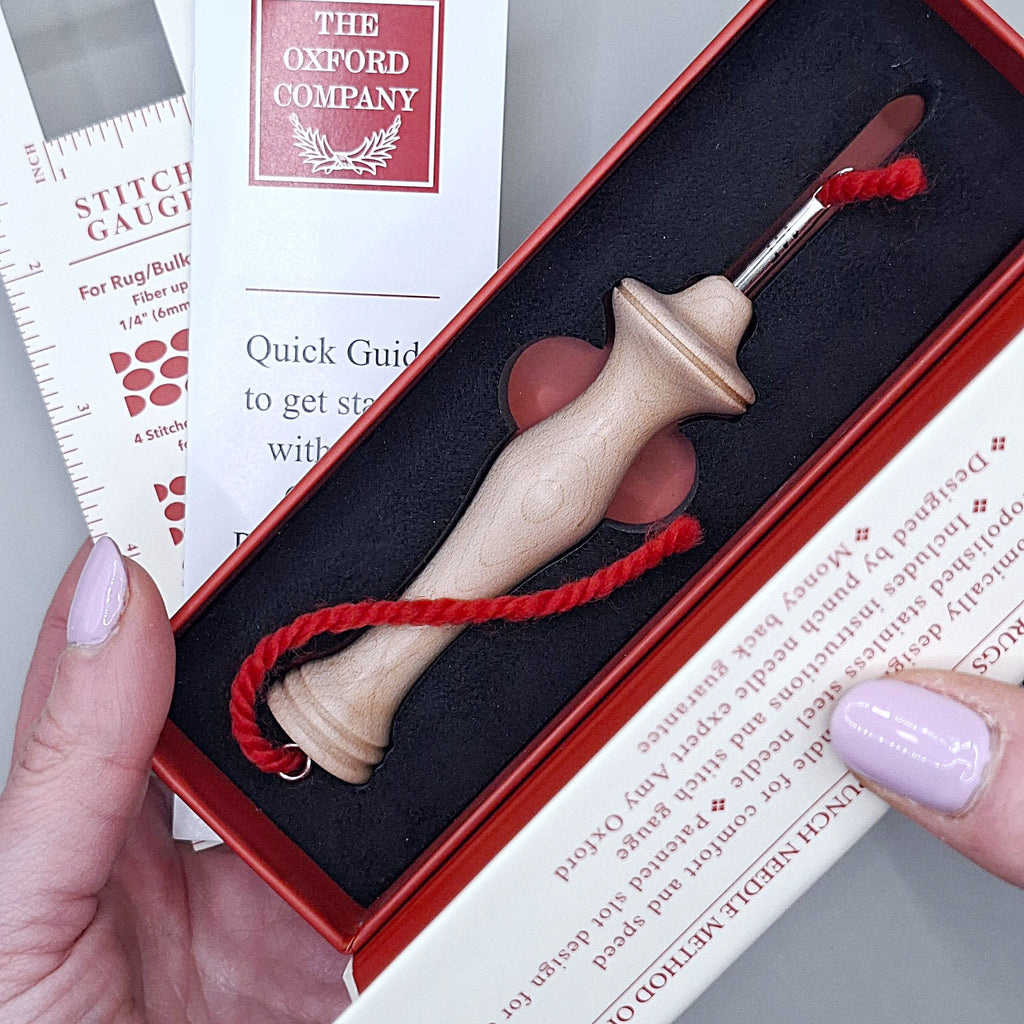 mani che sorreggono la scatola contenente un Oxford Punch Needle Fine, si nota anche un piccolo libricino di istruzioni e un righello