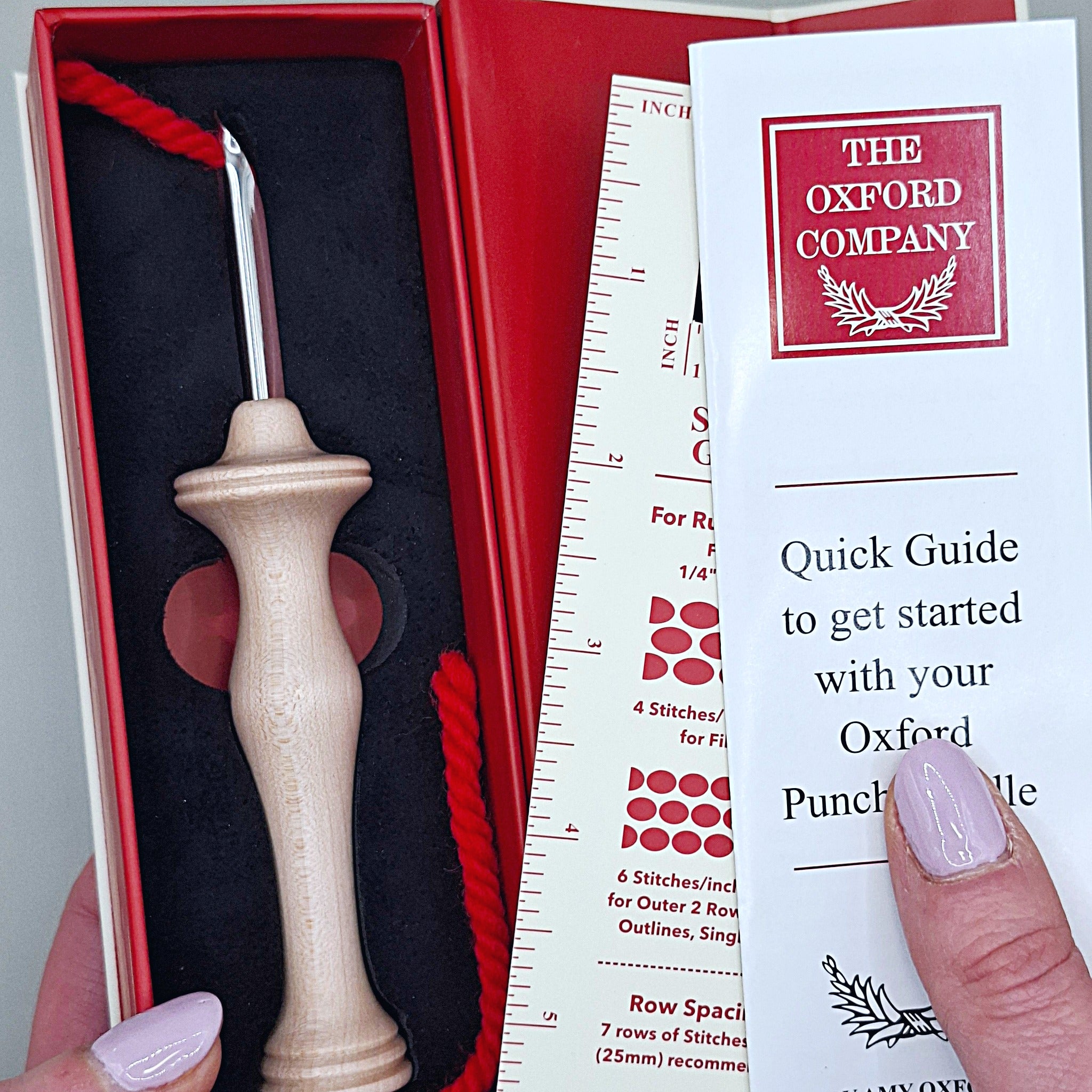 mani che sorreggono una scatola contenente un Oxford Punch Needle Regular, un piccolo libricino di istruzioni e un righello