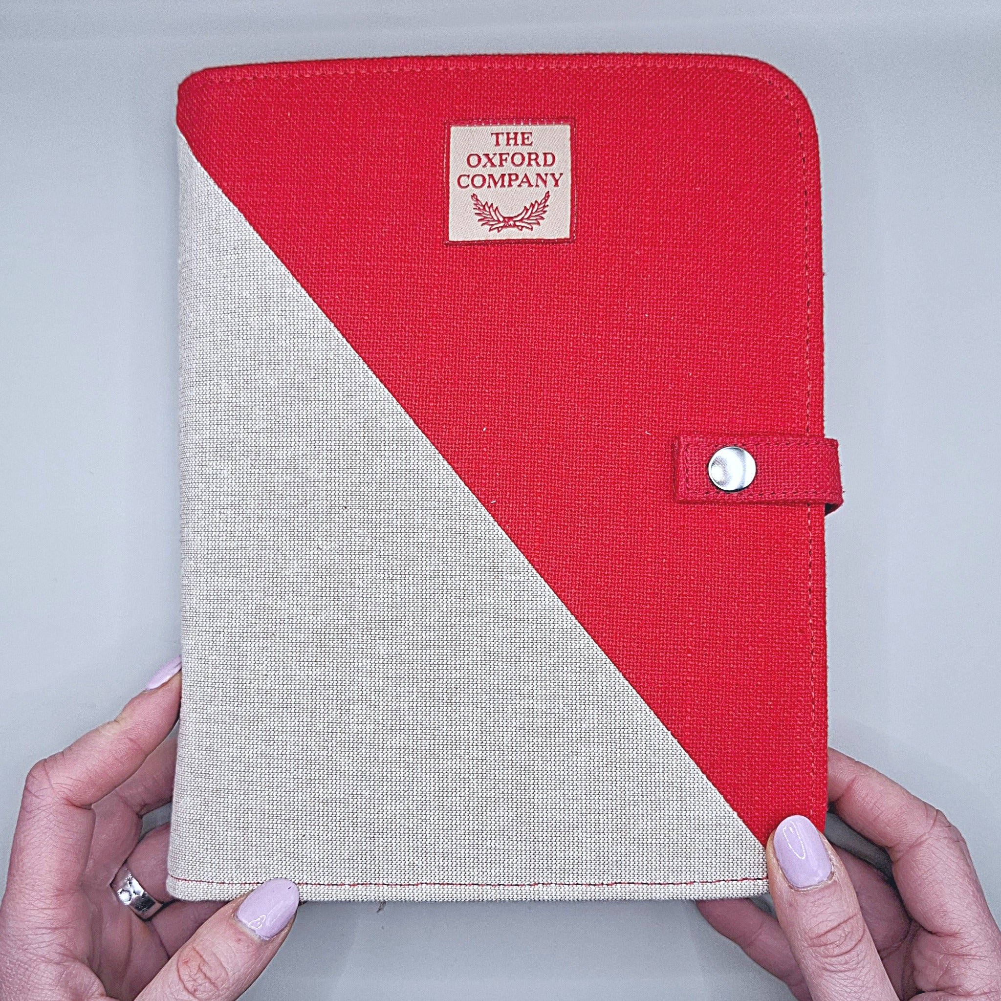 mani che sorreggono il cofanetto che è per metà rosso e per metà bianco panna, la divisione di colore è in diagonale, si vede il marchio The Oxford Company e un bottoncino a chiusura del cofanetto