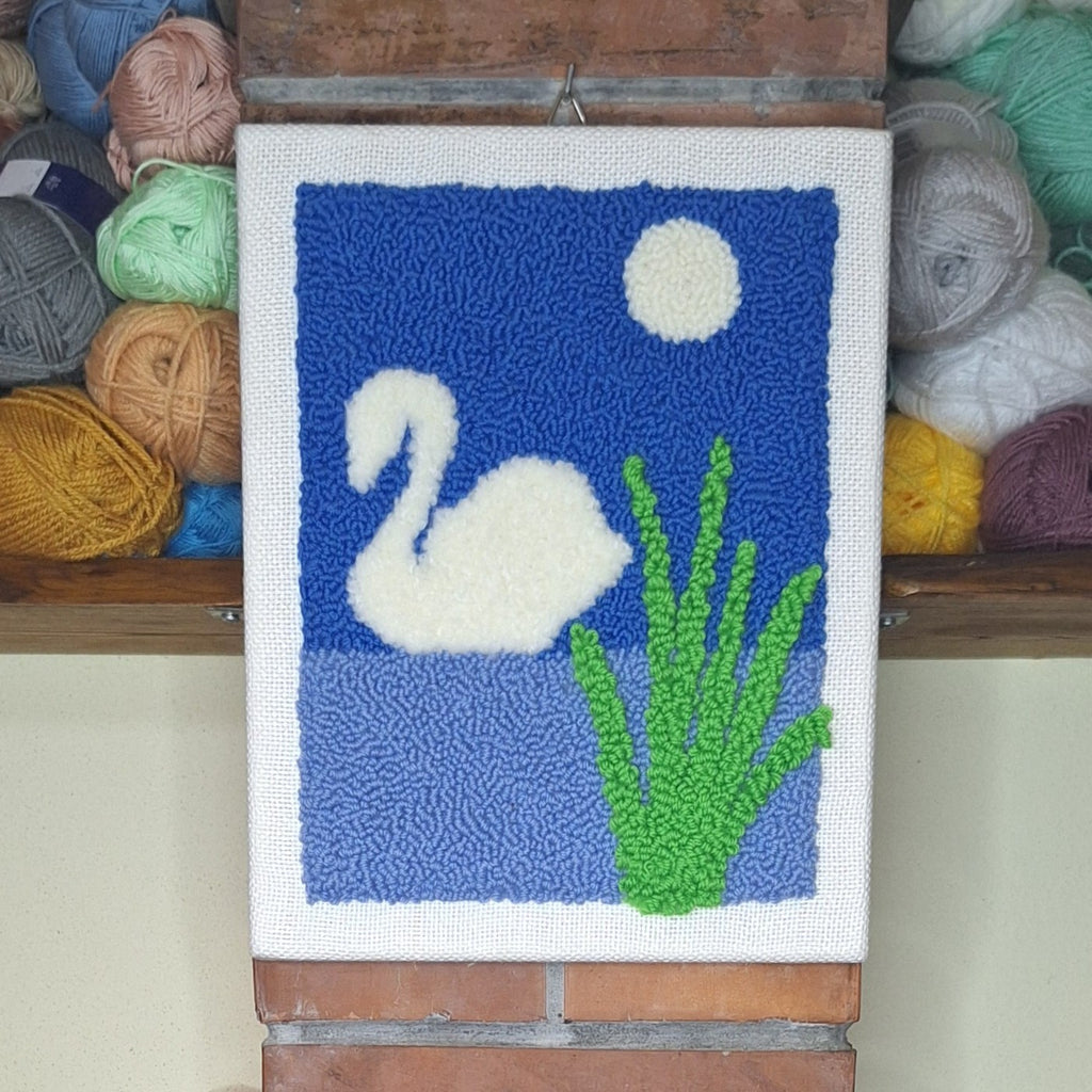 quadro ricamato con punch neelde appeso ad una colonna di muro. Si vedono sullo sfondo dei gomitoli. 